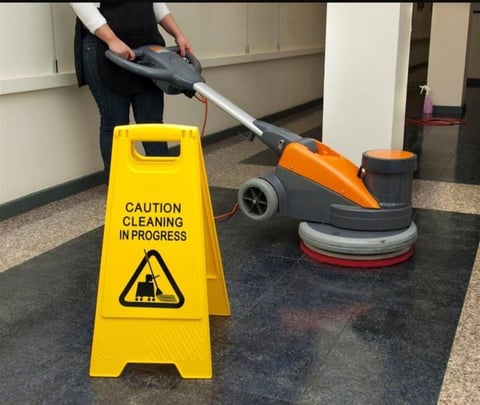 A floor cleaning machine with orange and black design and a yellow wet floor caution sign next to it during cleaning in progress