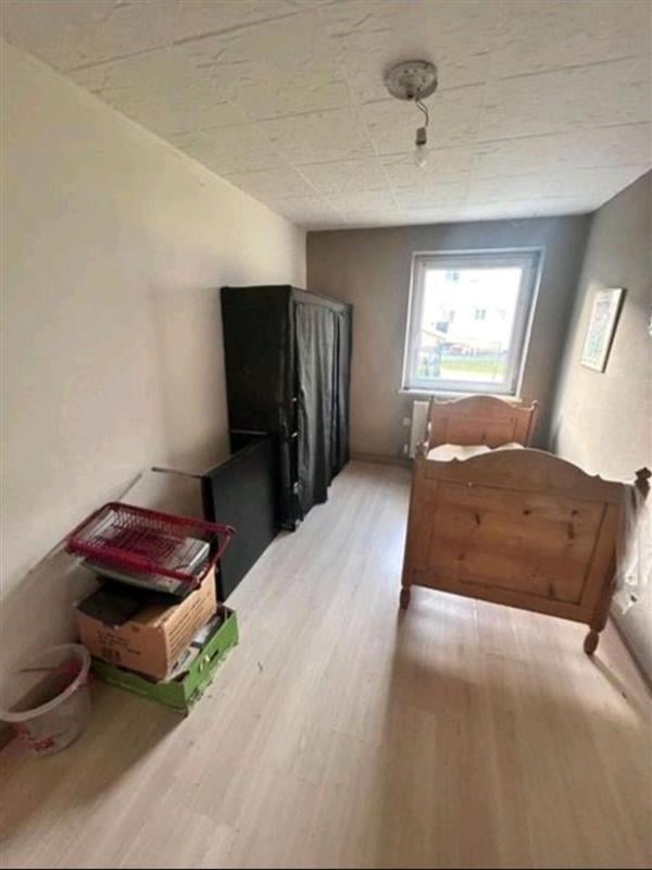 Sparse bedroom with wooden bed frame, black cabinet, storage boxes, window with natural light, and cream-colored ceiling