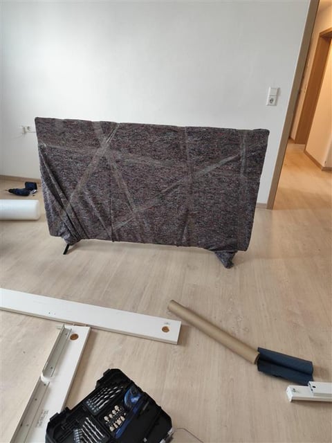 Gray fabric cover draped over furniture frame in empty room with assembly tools and materials on floor