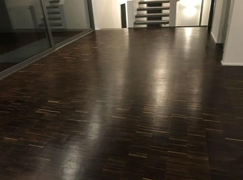 Empty modern loft space with dark hardwood floors, floor-to-ceiling windows, and white walls