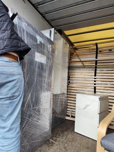 Worker loading plastic-wrapped furniture and bed frame into moving truck interior