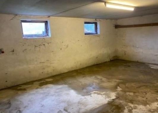 Empty basement room with yellow walls, stained concrete floor, and two small windows near the ceiling