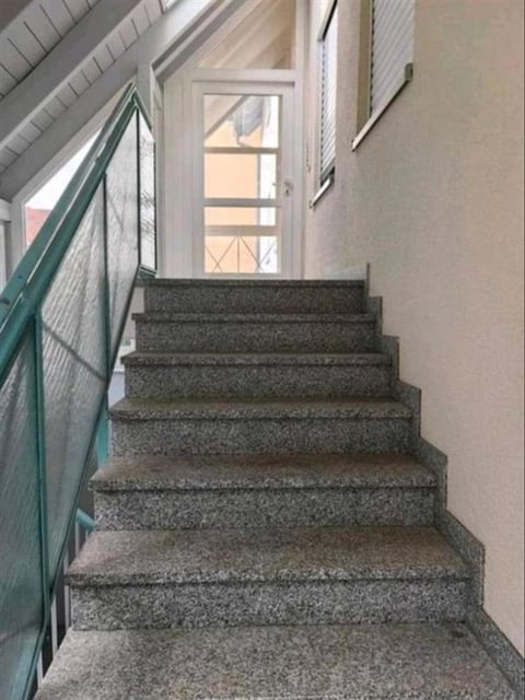 Gray carpeted staircase leading upward with white walls, green railing, and a window at the top