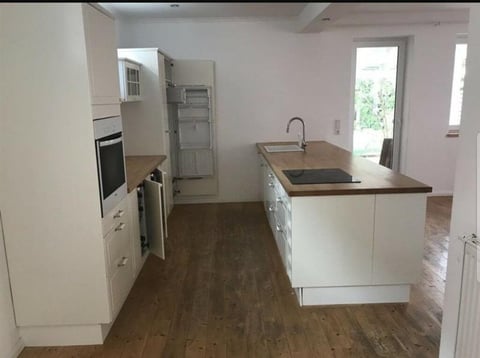 Modern kitchen with white cabinets, island counter, built-in appliances, and wood flooring