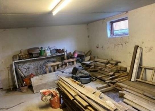 Cluttered basement or storage room with various wooden materials, furniture, and items scattered on the floor and shelves