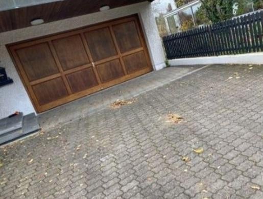 Brick paved driveway with brown wooden garage door and white house exterior with black fence